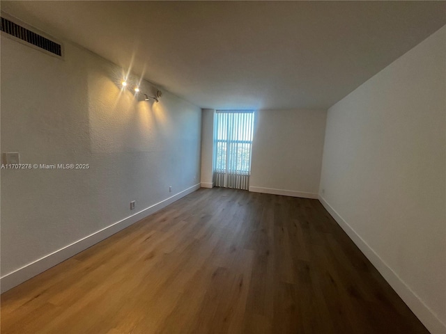 empty room featuring baseboards, wood finished floors, and visible vents