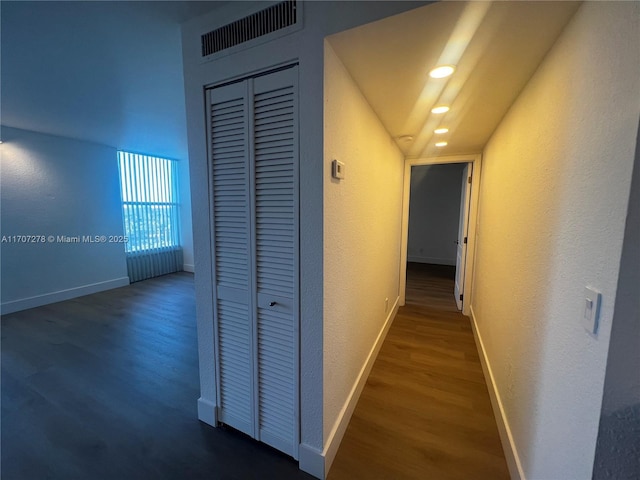 hallway with a textured wall, visible vents, baseboards, and wood finished floors