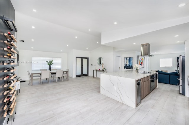 kitchen featuring island exhaust hood, light stone countertops, vaulted ceiling, black appliances, and a center island