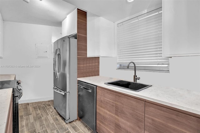 kitchen featuring appliances with stainless steel finishes, light wood-type flooring, light stone counters, sink, and white cabinetry