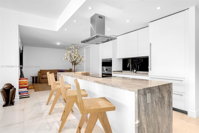 kitchen with white cabinetry, a breakfast bar area, black electric cooktop, island range hood, and a kitchen island