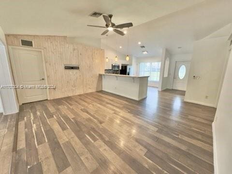 unfurnished living room with wood walls, dark hardwood / wood-style flooring, ceiling fan, and vaulted ceiling