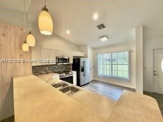 kitchen with appliances with stainless steel finishes, vaulted ceiling, sink, white cabinetry, and hanging light fixtures