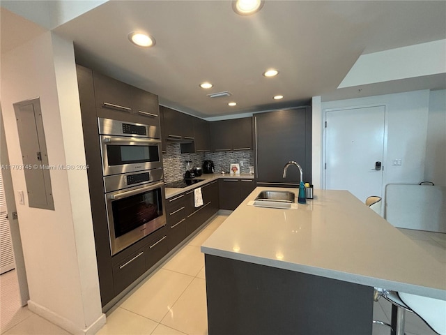 kitchen featuring sink, double oven, a breakfast bar area, black electric stovetop, and light tile patterned flooring