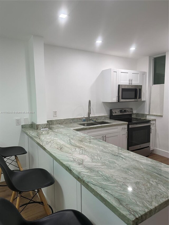 kitchen with sink, kitchen peninsula, light stone counters, white cabinetry, and stainless steel appliances