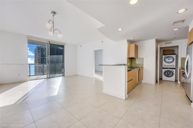 kitchen featuring light brown cabinets, hanging light fixtures, stacked washer / dryer, stainless steel fridge, and decorative backsplash