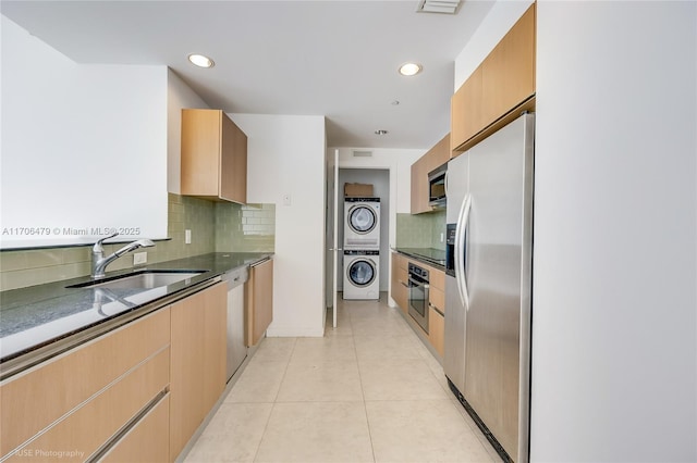 kitchen featuring sink, stacked washing maching and dryer, light tile patterned floors, tasteful backsplash, and stainless steel appliances