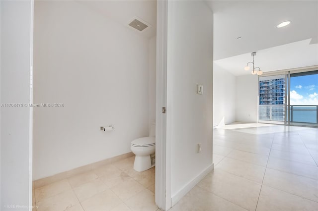 bathroom featuring tile patterned floors, expansive windows, a water view, an inviting chandelier, and toilet