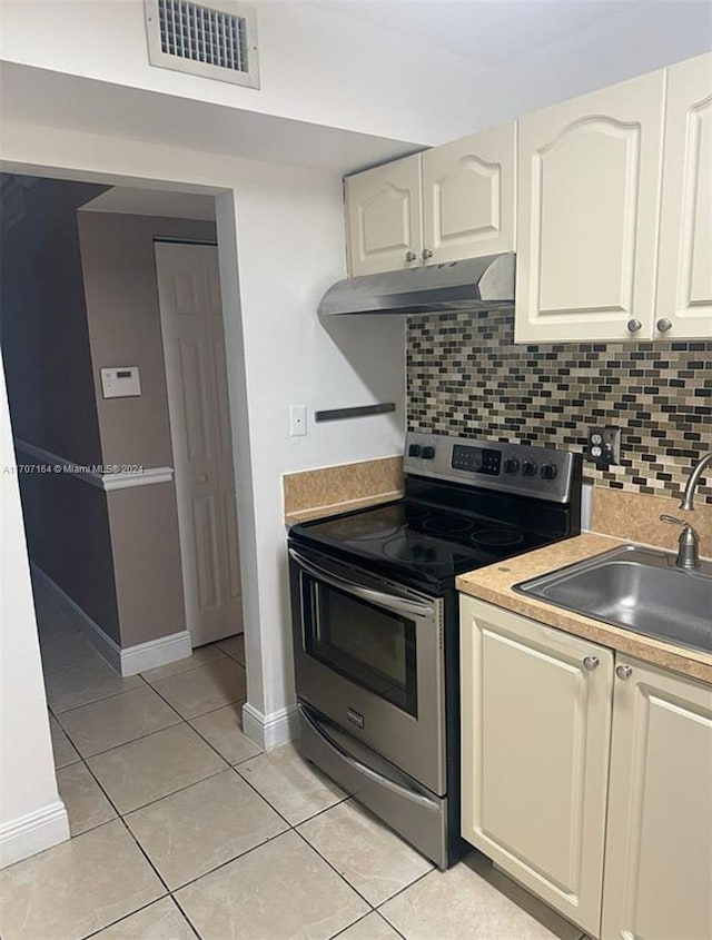 kitchen featuring stainless steel range with electric stovetop, decorative backsplash, light tile patterned flooring, and sink