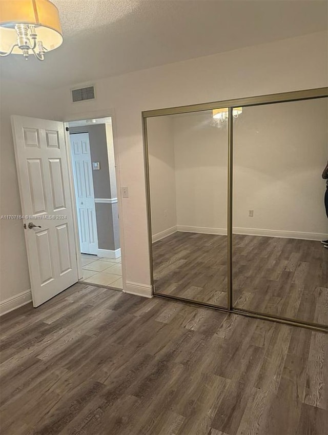 unfurnished bedroom with a textured ceiling, a notable chandelier, dark wood-type flooring, and a closet