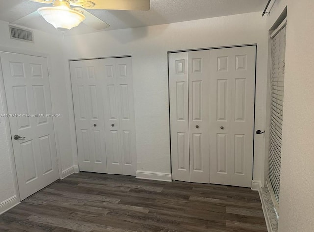 unfurnished bedroom with multiple closets, ceiling fan, and dark hardwood / wood-style floors