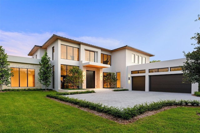 contemporary home with decorative driveway, an attached garage, a front lawn, and stucco siding