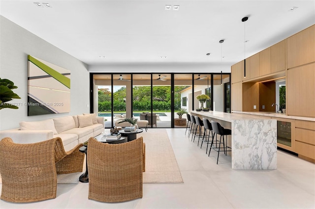 living room with ceiling fan, a wall of windows, sink, and wine cooler