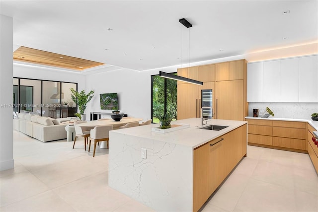 kitchen with light stone countertops, white cabinetry, sink, hanging light fixtures, and a center island with sink