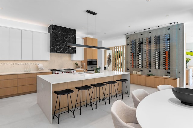 kitchen featuring sink, pendant lighting, extractor fan, a kitchen island with sink, and white cabinets