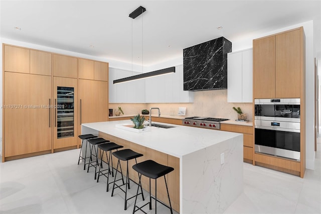 kitchen with stainless steel appliances, sink, white cabinets, an island with sink, and range hood