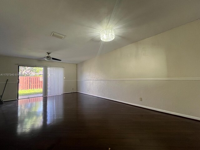 empty room featuring ceiling fan with notable chandelier and dark hardwood / wood-style flooring