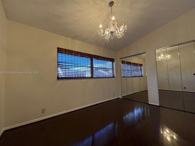 unfurnished bedroom featuring dark hardwood / wood-style floors, a chandelier, vaulted ceiling, a textured ceiling, and two closets