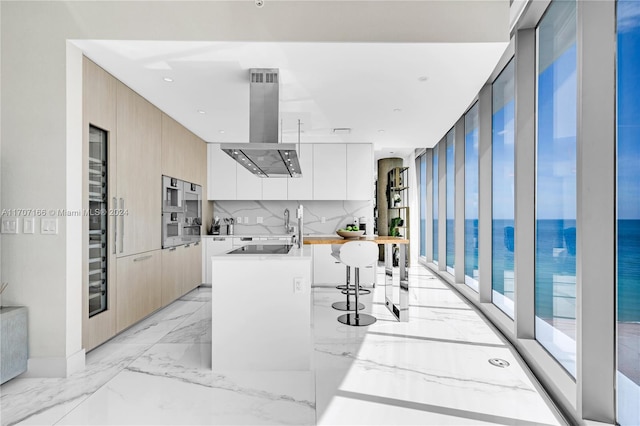 kitchen featuring exhaust hood, white cabinets, a kitchen breakfast bar, a water view, and an island with sink