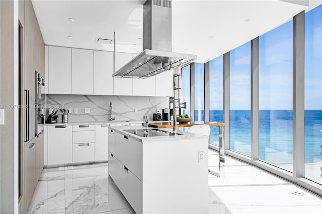 kitchen with a water view, white cabinets, island range hood, and an island with sink