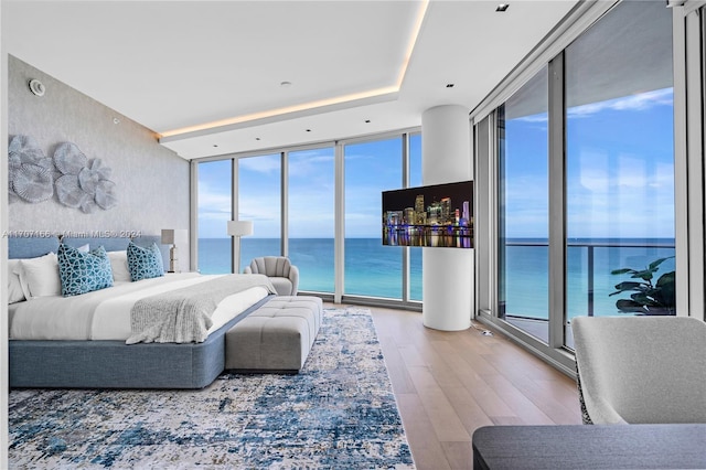 bedroom featuring access to outside, floor to ceiling windows, a water view, and hardwood / wood-style flooring