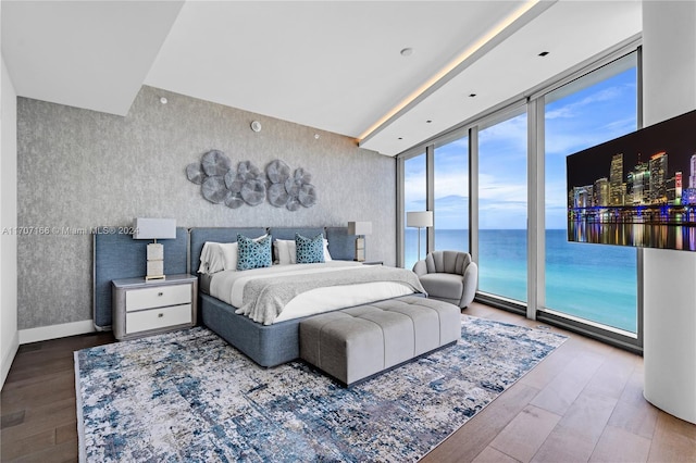 bedroom featuring access to outside, expansive windows, hardwood / wood-style floors, and a water view