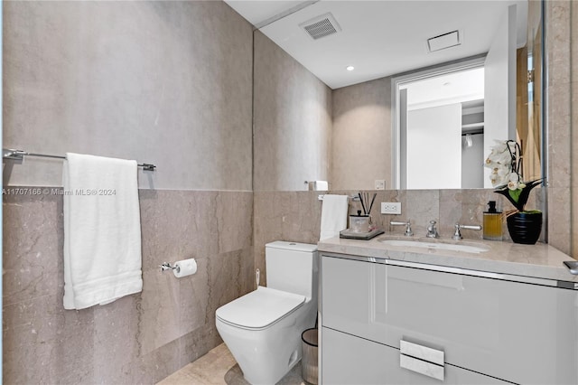 bathroom with tile patterned flooring, vanity, toilet, and tile walls