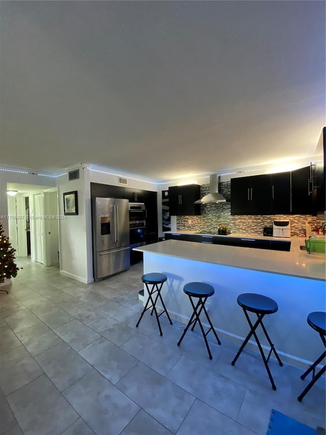 kitchen with a kitchen bar, kitchen peninsula, appliances with stainless steel finishes, and wall chimney range hood