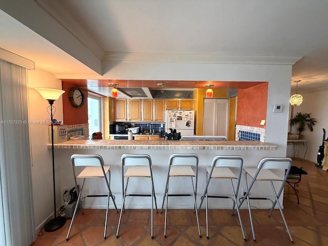 kitchen featuring a breakfast bar area, kitchen peninsula, backsplash, and white fridge