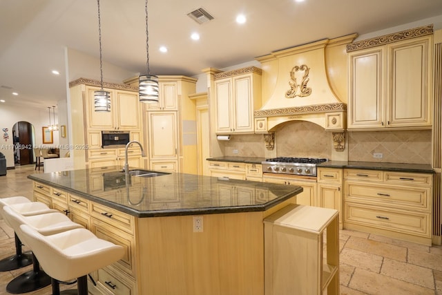 kitchen featuring sink, a kitchen island with sink, decorative light fixtures, custom exhaust hood, and stainless steel gas stovetop