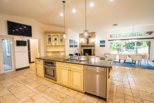 kitchen featuring lofted ceiling, sink, appliances with stainless steel finishes, a large fireplace, and a center island with sink