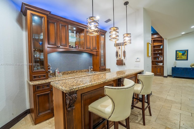 bar featuring light stone counters, hanging light fixtures, and sink