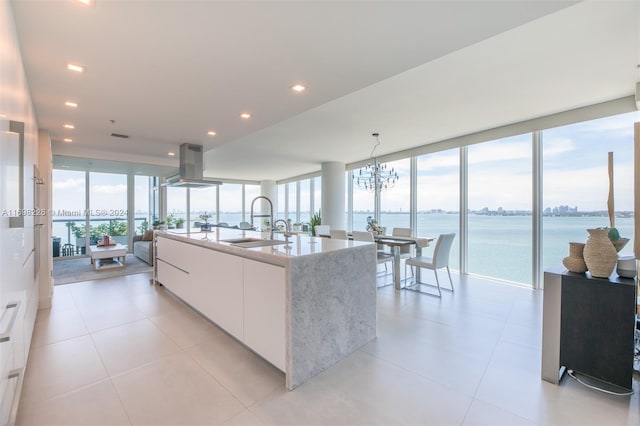 kitchen with white cabinetry, sink, an island with sink, island range hood, and a water view