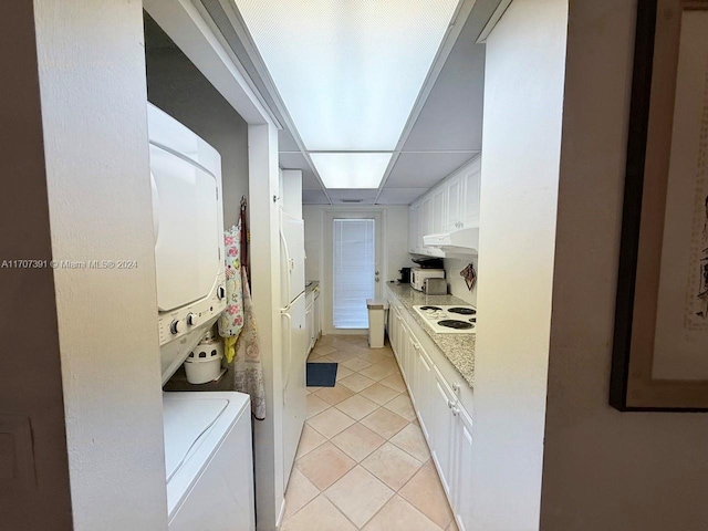 kitchen featuring white electric stovetop, light stone countertops, light tile patterned floors, stacked washer / drying machine, and white cabinetry