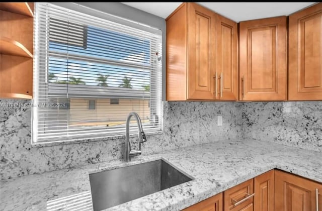 kitchen with backsplash, light stone countertops, and sink