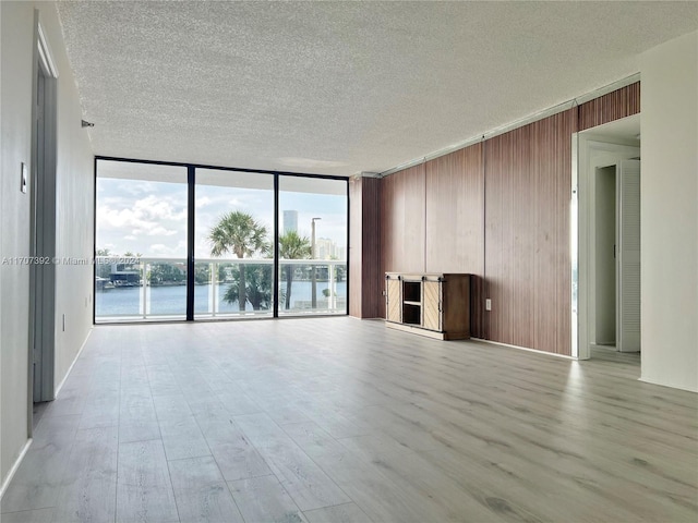 unfurnished living room with a textured ceiling, light hardwood / wood-style floors, expansive windows, and a water view