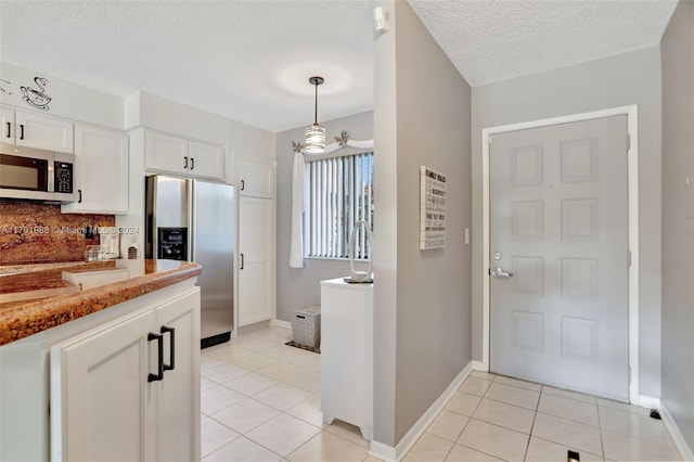 kitchen featuring white cabinetry, stainless steel appliances, light stone counters, a textured ceiling, and light tile patterned flooring