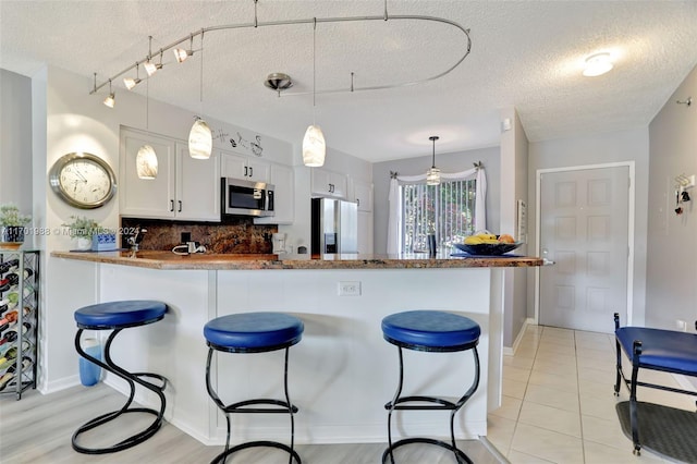 kitchen with a textured ceiling, white cabinets, kitchen peninsula, and stainless steel appliances