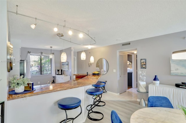 kitchen featuring light stone countertops, light wood-type flooring, a breakfast bar, a textured ceiling, and pendant lighting