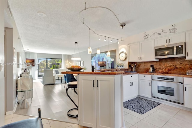 kitchen with white cabinetry, stainless steel appliances, kitchen peninsula, a textured ceiling, and decorative light fixtures