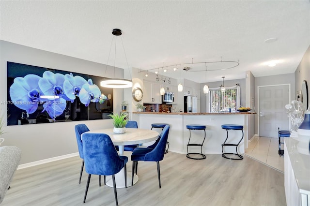 dining area featuring rail lighting, a textured ceiling, and light hardwood / wood-style flooring