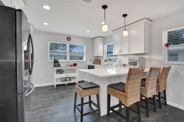 kitchen featuring white cabinets, stainless steel fridge, kitchen peninsula, and hanging light fixtures