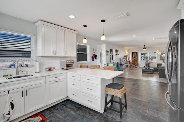 kitchen with kitchen peninsula, a breakfast bar, pendant lighting, white cabinetry, and stainless steel refrigerator