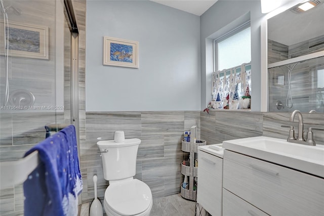 bathroom with vanity, toilet, a shower with shower door, and tile walls