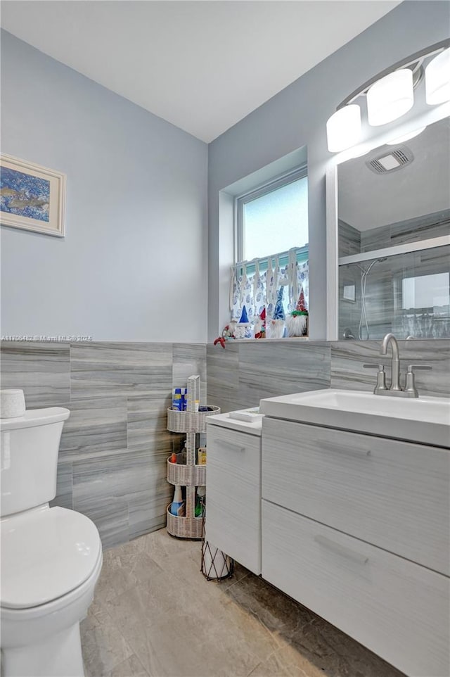 bathroom with vanity, a shower with door, toilet, and tile walls