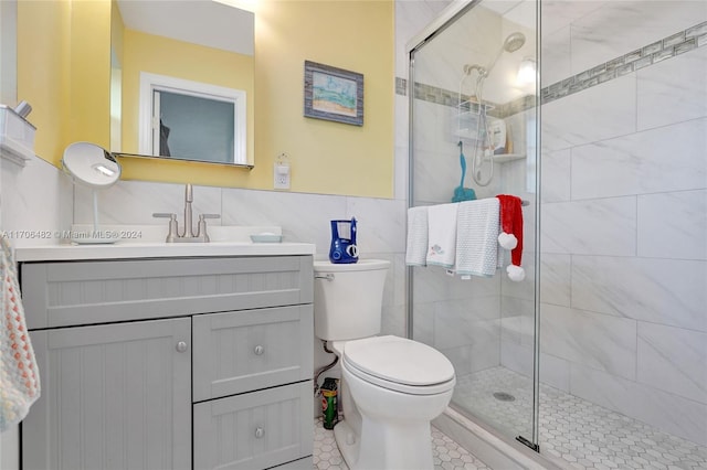 bathroom with tile patterned floors, toilet, a shower with door, vanity, and tile walls