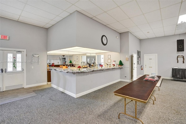 kitchen with a drop ceiling, kitchen peninsula, a towering ceiling, a kitchen bar, and dark carpet