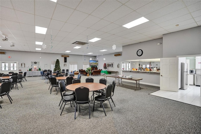 dining space featuring a paneled ceiling, light colored carpet, and a high ceiling