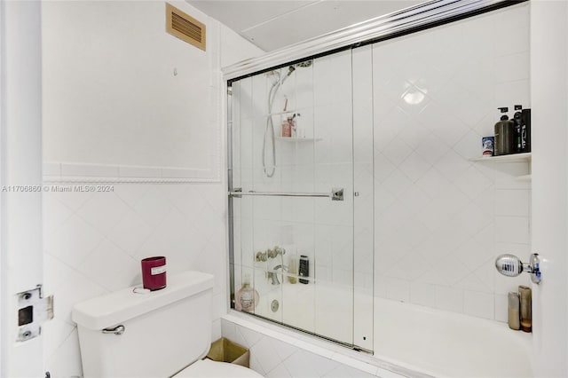 bathroom featuring toilet, shower / bath combination with glass door, and tile walls