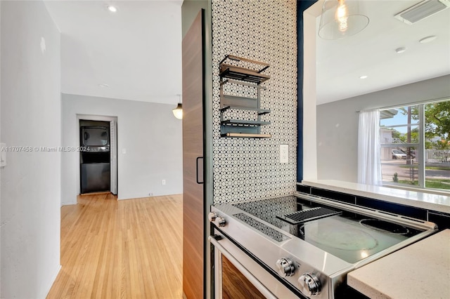 kitchen with decorative backsplash, pendant lighting, light wood-type flooring, and stainless steel stove